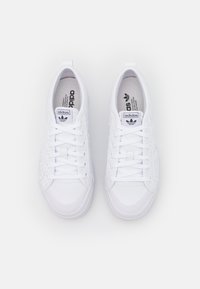 Vita atletiska sneakers i vit färg med vävd textur och läderdetaljer, rund tå, platta sulor och snörning. Logotyp synlig på tungan.