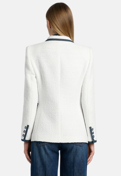 Witte, gestructureerde blazer met een getailleerde pasvorm, voorzien van een contrasterende marineblauwe kraag en knoopmanchetten, gecombineerd met donkere spijkerbroeken.