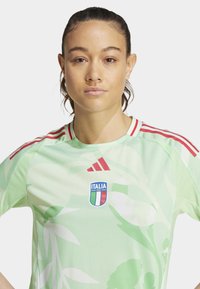 Svetlozelena nogometna majica z rdečimi akcenti. Ima cvetlični vzorec in na sprednji strani logotip italijanske reprezentance. Narejena je iz dihalnega materiala.
