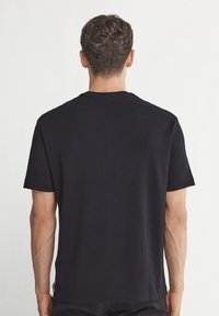 Svart t-shirt med kort ärm i mjuk bomull, med klassisk rund hals och rak skärning, med minimala sömmar och inga tryck.