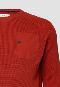 Maglione rosso a maglia con finitura testurizzata, colletto a coste e taschino con un bottone blu. Il marchio è visibile sulla tasca.