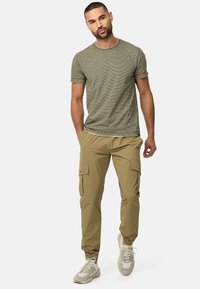 Olivengrøn mønstret t-shirt med korte ærmer, khaki cargo bukser med sidelommer og lysegrå sneakers med teksturerede detaljer.