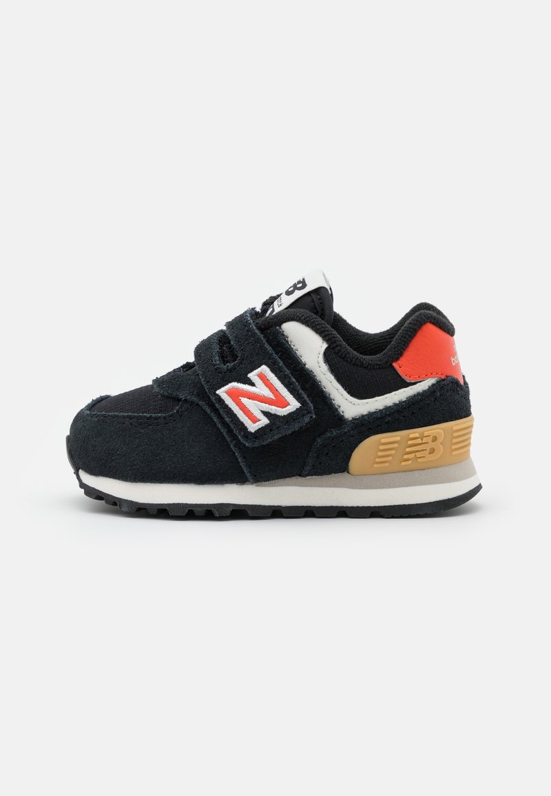 Baskets bébé noir et blanc avec accents rouges, fermeture velcro et un soutien de talon beige marqué "NB" sur fond blanc.