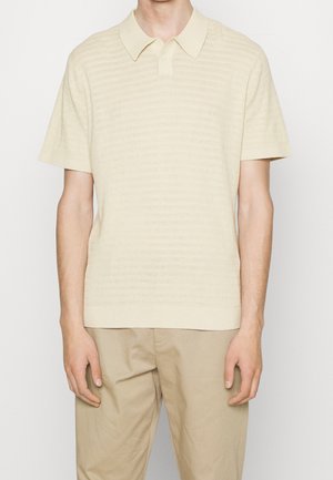 Polo tričko s krátkým rukávem v světle béžové barvě s jemnými horizontálními pruhy, pletená textura a skládací límec. V kombinaci s khaki kalhotami.