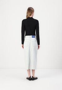 Crna bluza dugih rukava uparena s svijetloplavom traper midi suknjom, koja ima sirovi rub i HUGO logotip na stražnjoj strani. Crna obuća upotpunjuje izgled.