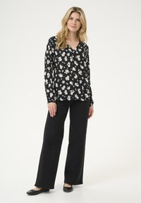 Blusa nera a maniche lunghe con design a scollo a V, fantasia floreale chiara, abbinata a jeans neri a gamba larga e ballerine nere.