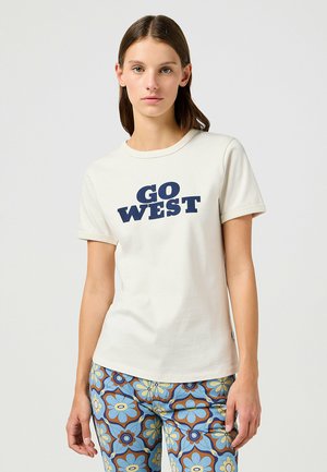 Cremefarvet bomulds T-shirt med korte ærmer, prydet med marineblå "GO WEST" tekst. Sammen med mønstrede blå og brune blomsterbukser.
