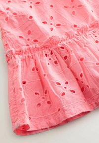 Rosa bomullsklänning med broderade blommönster och utskurna detaljer, med en samlad volangnederkant och texturerad yta.