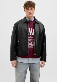 Schwarze Lederjacke mit durchgehendem Reißverschluss, mit einem Kragen-Halsbereich und zwei seitlichen Taschen. Über einem bordeauxfarbenen Sweatshirt getragen.