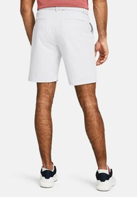 Weiße Shorts aus glattem Stoff mit zwei Gesäßtaschen. Getragen mit weißen und marineblauen Turnschuhen, die ein kurz geschorenes, behaartes Bein zeigen.