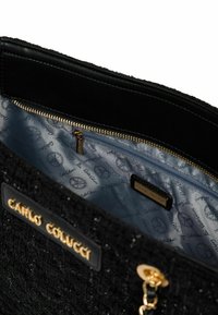 Schwarze, strukturierte Handtasche mit einem goldenen Reißverschluss und Logo-Akzenten, innen mit einem blauen Futter, das mit dem Markennamen gemustert ist.