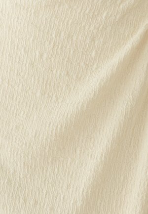 Tissu de couleur crème avec un motif texturé subtil comportant de petites lignes verticales et horizontales en relief, créant un effet de grille douce.