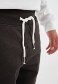 Svarta joggers med ribbad midja, vit dragsko och metallaglets. Tyget verkar mjukt och texturerat. Hand synlig på sidan.