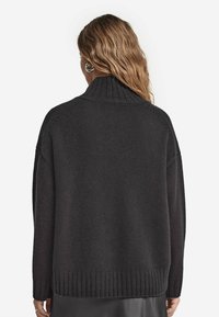 Mörkgrå oversized tröja med hög krage, ribbad nederkant och texturerad stickad mönster. Bakifrån syns sänkta axlar och lös passform.