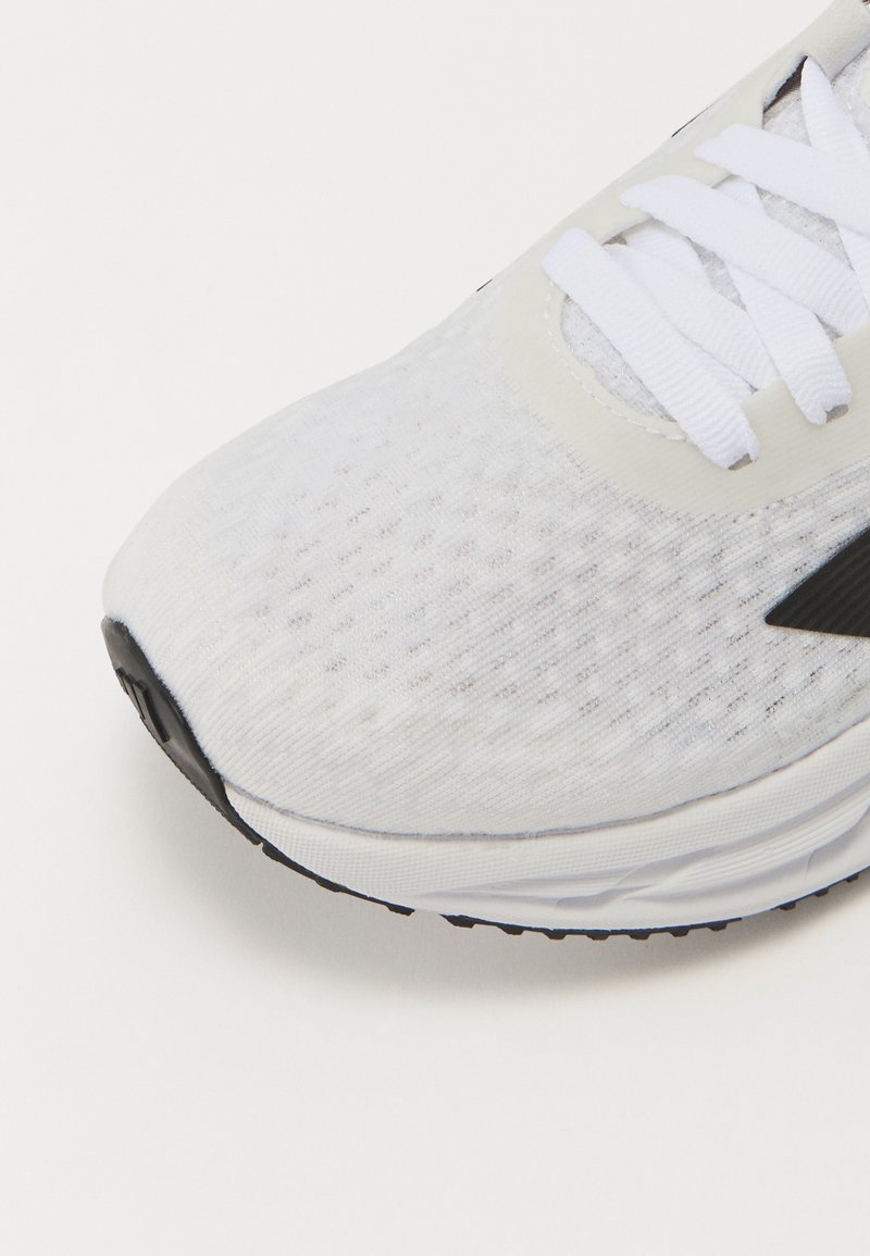 Scarpa atletica bianca con tomaia in rete texture, lacci bianchi piatti e suola in gomma nera; presenta un punta liscia e una logo discreta.