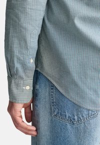 Grüne und marineblaue karierte Hemd mit langen Ärmeln, kontrastierenden weißen Knöpfen, getragen mit hellblauen Jeans.