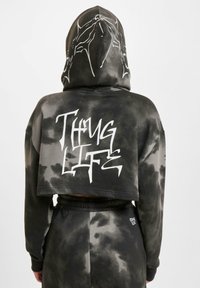 Strihaná čierna mikina s kapucňou a šedým tie-dye vzorom. Na zadnej strane má grafický biely potlač s nápisom "Thug Life" a šnúrku na kapucni.