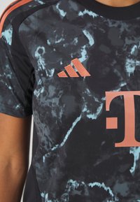 Musta urheilupaita, jossa on marmoroitu kuosi sinisillä yksityiskohdilla, brodeerattu oranssi Adidas-logo ja suuri oranssi "T" -grafiikka.