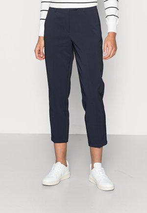 Personne portant un pantalon bleu marine raccourci à jambes droites, des baskets blanches et un haut blanc à manches longues avec des rayures horizontales noires.