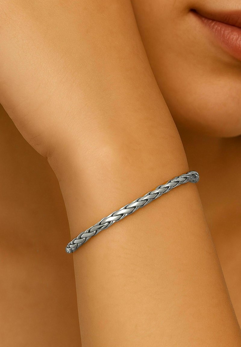 Bracciale intrecciato in argento poggiato su un braccio nudo, con una finitura metallica liscia e un design intrecciato.