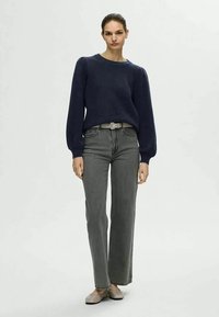 Maglione lavorato a maglia blu navy con maniche a sbuffo, abbinato a jeans grigi a gamba dritta e vita alta e ballerine di colore chiaro, completato con una cintura semplice.
