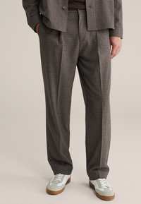 Spodnie od garnituru w kratę w ciemnoszarym kolorze z jasnymi akcentami, o luźnym kroju i zakładkach. Połączone z białymi i szarymi trampkami.