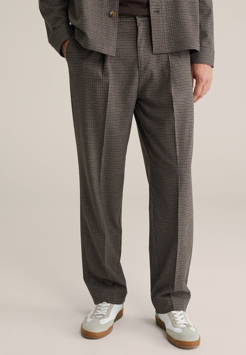 Spodnie od garnituru w kratę w ciemnoszarym kolorze z jasnymi akcentami, o luźnym kroju i zakładkach. Połączone z białymi i szarymi trampkami.