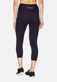 Fekete, térd fölé érő leggings rugalmas anyagból, széles derékpánttal, amelyen a "Winshape" felirat található. Strukturált, testhezálló kialakítás.