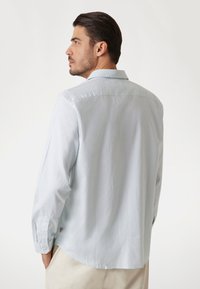 Camicia a maniche lunghe a righe blu chiaro con colletto standard, polsini abbottonati e orlo dritto. Il tessuto appare liscio e leggero.