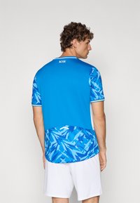 Camiseta atlética azul com padrões geométricos abstratos, mangas curtas e costas lisas. Apresenta detalhes brancos e o logótipo "KYIV" na gola.