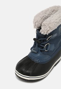 Bota de inverno azul-marinho com uma base de borracha preta, textura de aderência, colarinho de pele sintética e fecho de atacadores ajustável. Apresenta um forro suave e isolado.