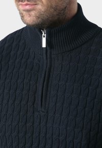 Granatowy sweter dzianinowy z wysokim kołnierzem i zapięciem na pół-zamek. Posiada wzór w warkocze, teksturowany design oraz gładką metalową suwaki.