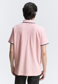 Kurzärmliges Poloshirt aus leichtem rosa Baumwollstoff, mit einem marineblauen Kragenrand und seitlichen Schlitzen am Saum für mehr Bewegungsfreiheit.