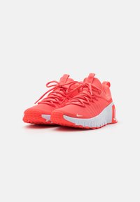 Pantofi sport strălucitori de culoare corali, cu un superior texturat, talpă albă și un design flexibil. Prezentă sistem de șireturi și un logo pe lateral.