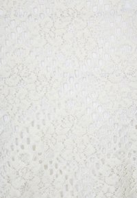 Krajková tkanina v barvě slonové kosti s květinovými a geometrickými vzory, která má jemnou, poloprůhlednou strukturu a složité detaily prošívání.