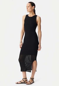 Czarna dzianinowa sukienka prążkowana o dopasowanym kroju, z bocznymi rozcięciami i dolnym półprzezroczystym panelem. W połączeniu z czarnymi sandałami z ćwiekami.