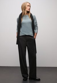 Lyseblå, tekstureret sweater med lange ærmer kombineret med mørke, løstsiddende bukser. Sorte sko fuldender outfittet.