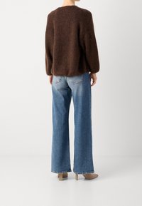 Braun, flauschiger Strickpullover mit langen Ärmeln, kombiniert mit hellblauen weit geschnittenen Jeans und beigen Absätzen. Rückansicht, die Textur und Passform zeigt.