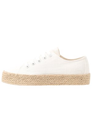 White canvas sneaker with a textured finish, featuring a woven jute sole, round toe, and six eyelets with metallic eyelets.