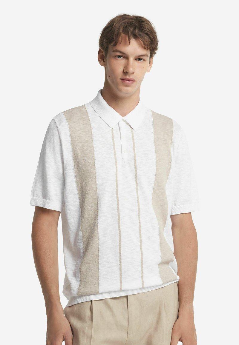 Kortärmad polo i vitt och beige med vertikala ränder, klassisk krage och texturerat tyg. Har en avslappnad passform och ribbade ärmslut.