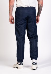 Marineblauwe sportbroek met een elastische tailleband en boorden, gemaakt van een gladde, lichte stof en voorzien van zijzakken.