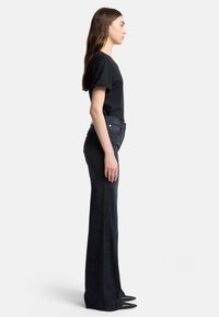 T-shirt nera con maniche arrotolate, abbinata a jeans in denim scuro a palazzo. L'outfit presenta un design elegante e una silhouette aderente.