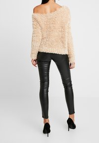 Beige, načechraný svetr bez ramínek s dlouhými rukávy, zkombinovaný s černými legínami z umělé kůže a černými lodičkami na vysokém podpatku.