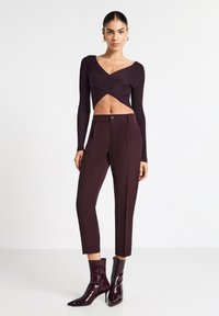 Top corto a maniche lunghe ribbed borgogna abbinato a pantaloni a vita alta aderenti e stivaletti lucidi alla caviglia, che mettono in risalto un'elegante silhouette.
