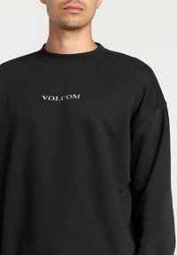 Black sweatshirt made from soft fabric, featuring a crew neckline and a white "VOLCOM" logo across the chest. Relaxed fit, visible stitching.