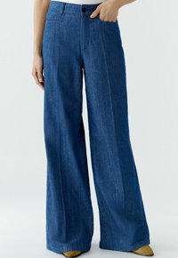 Weite Jeans mit mittlerem Blauton, bestehend aus einem glatten Material, hoher Taille und vorderen Taschen. Abgerundet mit kontrastierenden Nähten.