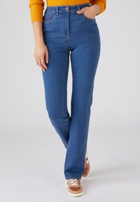 Jean en denim bleu avec une coupe droite, taille haute et cinq poches. Associé à des baskets marron et blanches.