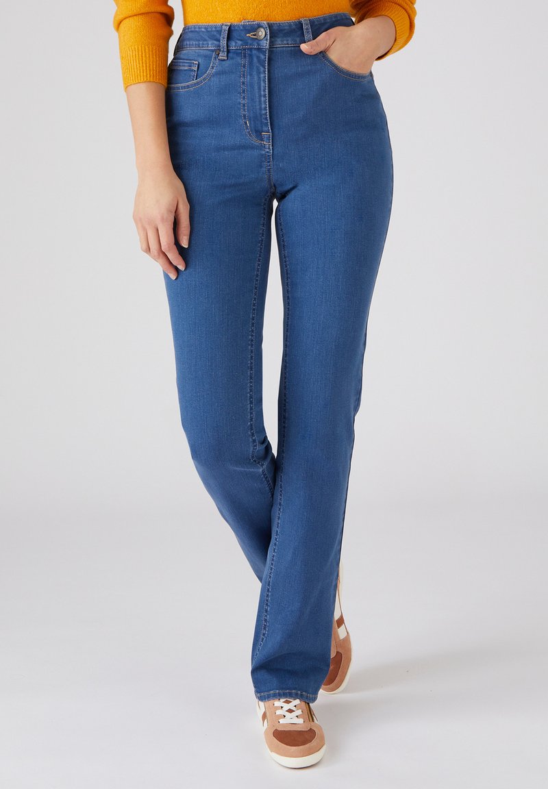 Jean en denim bleu avec une coupe droite, taille haute et cinq poches. Associé à des baskets marron et blanches.