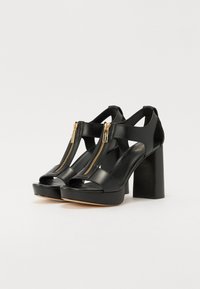 Sandale negre din piele cu toc chunky, cu vârf deschis și două detalii cu fermoar în față. Textură netedă cu talpă platformă și accente din metal aurit.