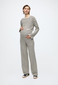 Csíkos krémszínű és fekete kötött pulóver és bő szárú nadrág szett, puha textúrával és hosszú ujjakkal. Fekete és krémszínű cipőkkel párosítva.